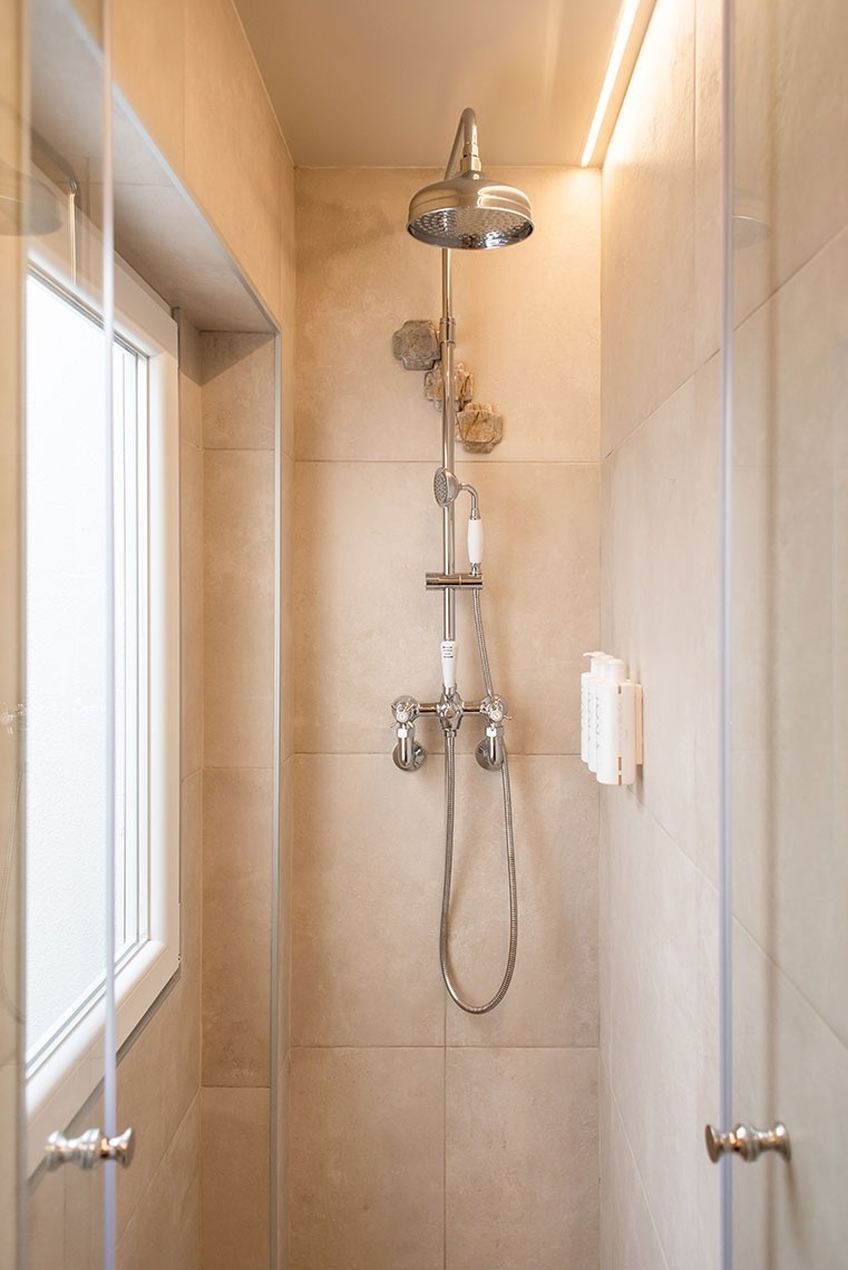 Chuveiro de hotel moderno com ducha cromada, azulejos bege e iluminação ambiente.
