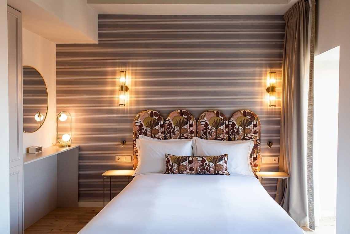 Quarto de hotel elegante com cama confortável, cabeceira estampada e iluminação acolhedora.