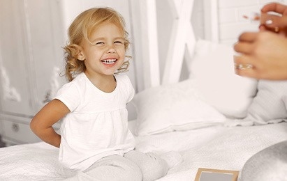 a little girl is sitting on a bed and smiling .