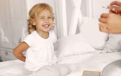 una niña está sentada en una cama sonriendo y mirando a la cámara .