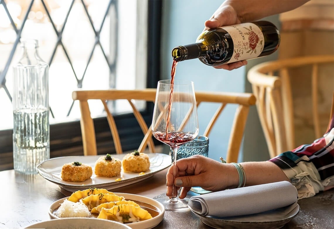 una persona sostiene una botella de vino y lo vierte en un vaso