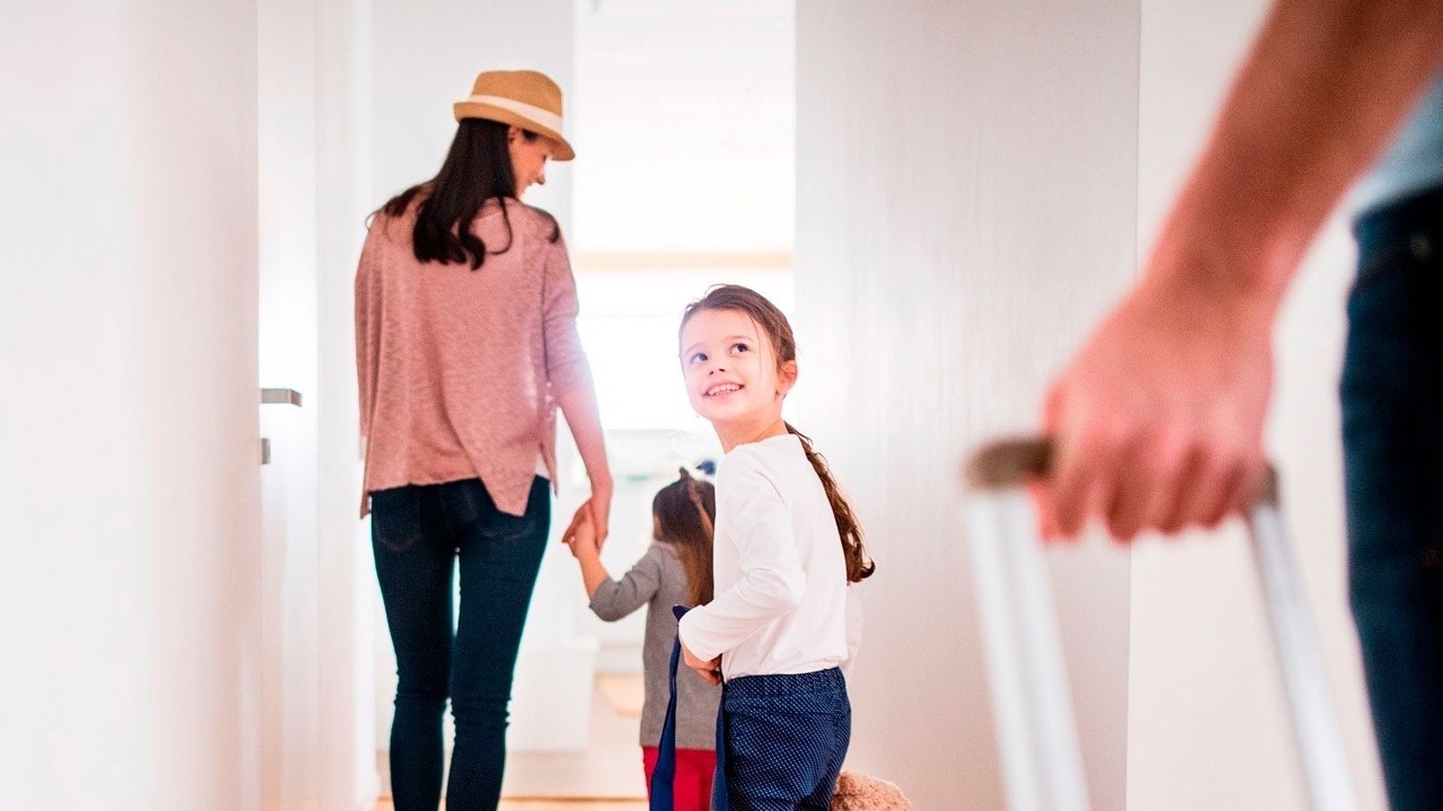 a woman in a hat holds hands with two little girls while a man holds a suitcase