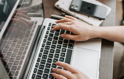 una persona está sentada en una mesa usando una computadora portátil y un teléfono inteligente .