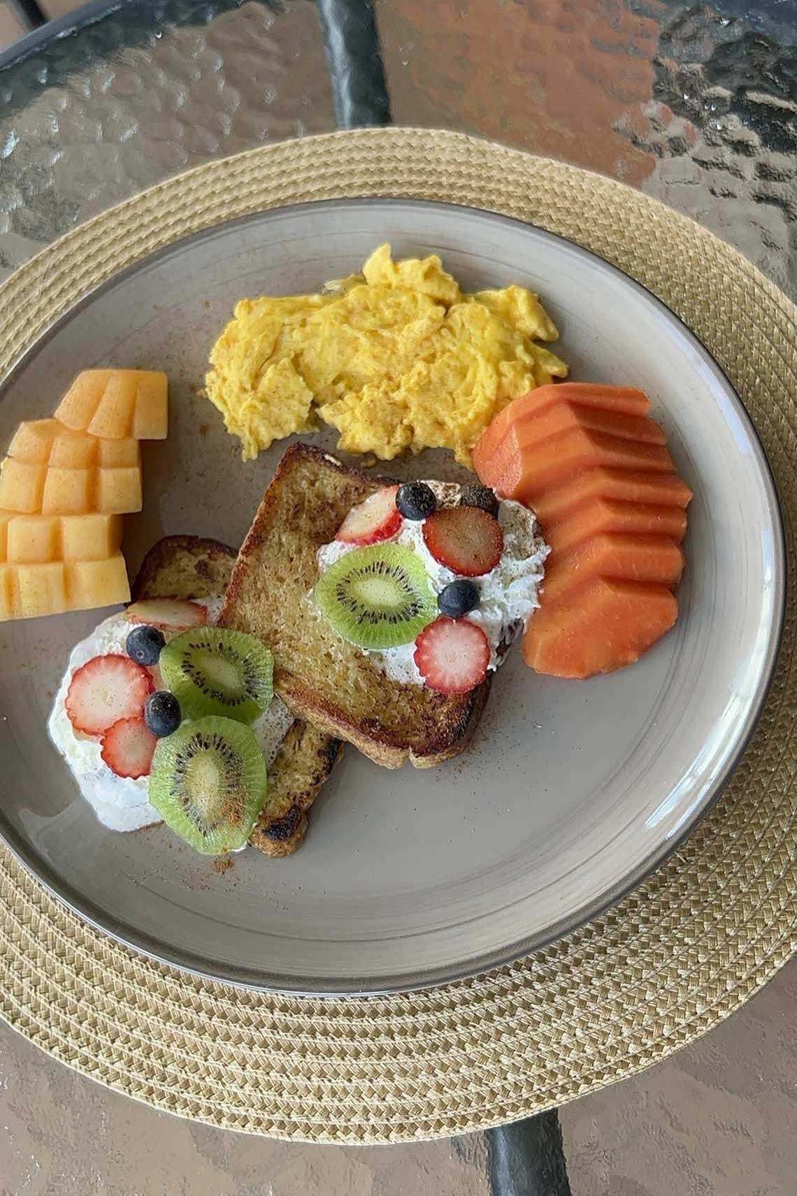 un plato de desayuno con huevos revueltos tostadas kiwi fresas y melón