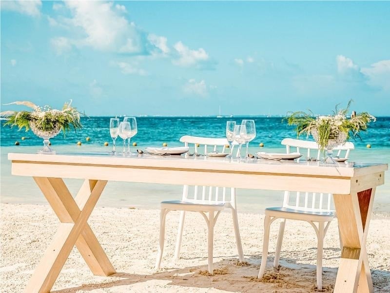 una mesa de madera con sillas y copas de vino en la playa