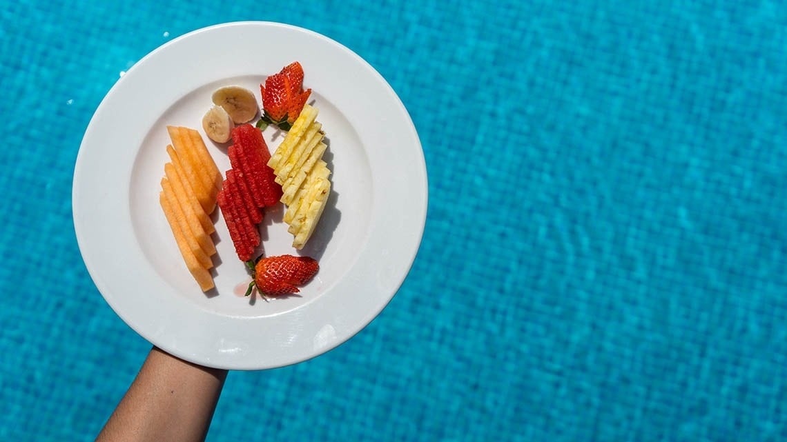 a person is holding a plate of fruit in front of a pool