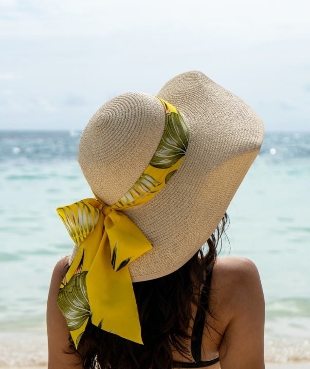 una mujer con un sombrero de paja y una cinta amarilla está sentada en la playa