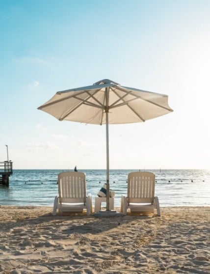 two chairs under an umbrella on the beach near the ocean