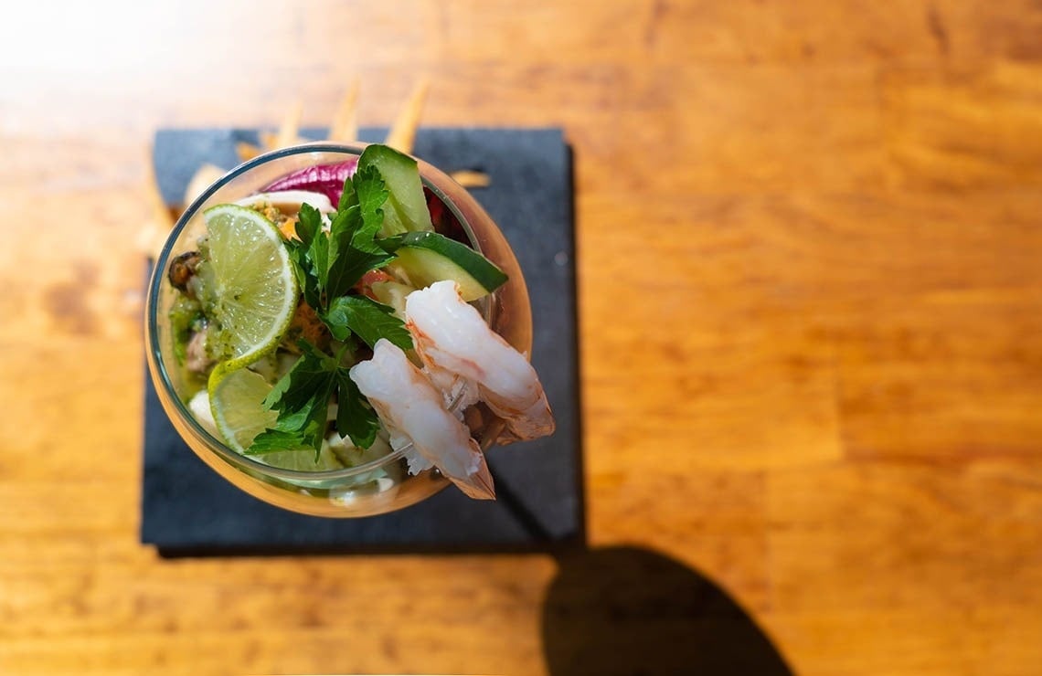 a glass filled with shrimp and vegetables on a table