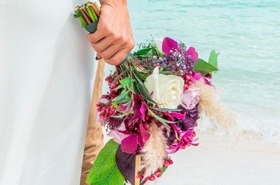 una novia sostiene un ramo de flores en la playa .