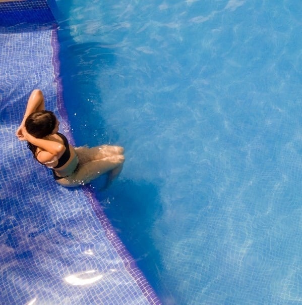 una mujer se sienta en el borde de una piscina azul