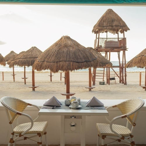 a table and chairs on the beach with a lifeguard tower in the background