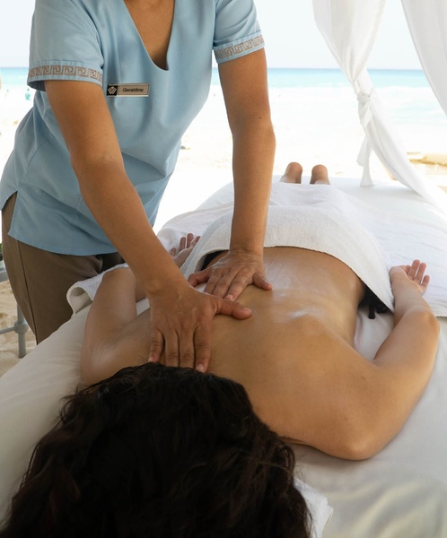 una mujer recibe un masaje en la playa mientras lleva una camisa azul con la palabra masajeador