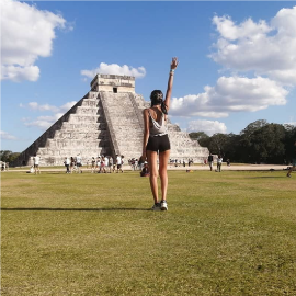 una mujer se para en un campo de hierba frente a una pirámide antigua