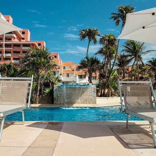 a swimming pool with chairs and umbrellas and a waterfall in the background