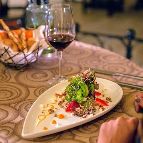 a woman sits at a table with a plate of food and a glass of wine