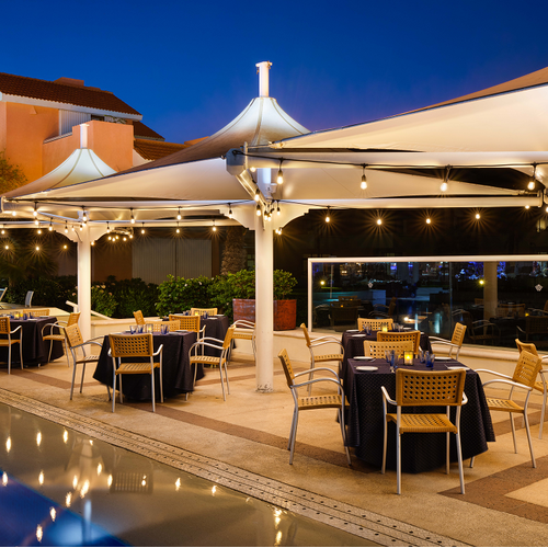 tables and chairs under umbrellas near a pool at night