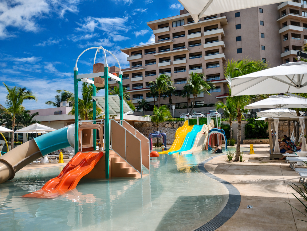 Piscina infantil en Wyndham Grand Cancun, con toboganes, fuentes y camastros.