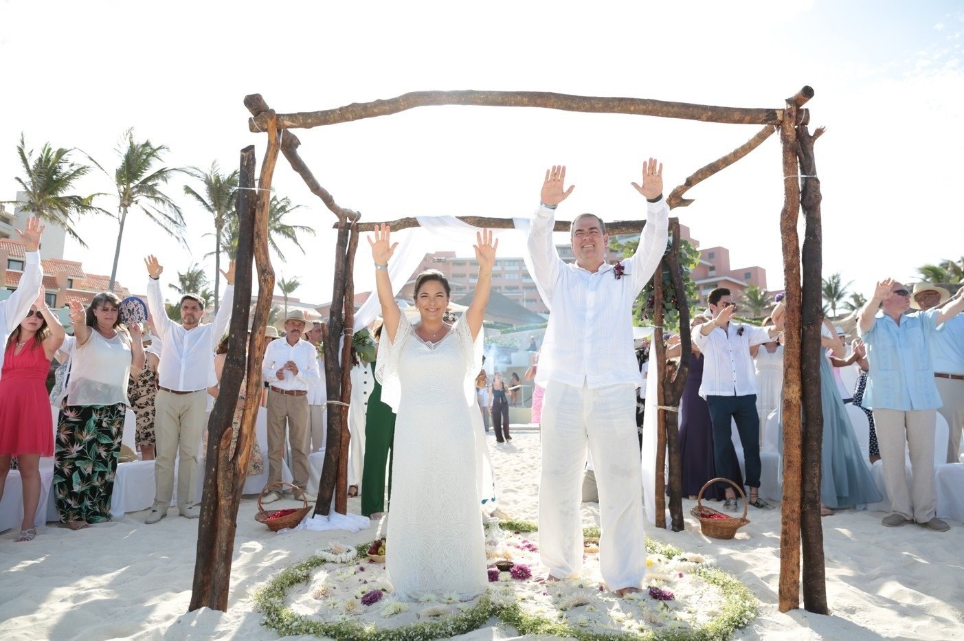 a bride and groom stand in front of a circle of flowers on the beach