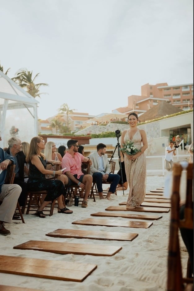 una novia y un novio se besan en la playa frente a un arco floral