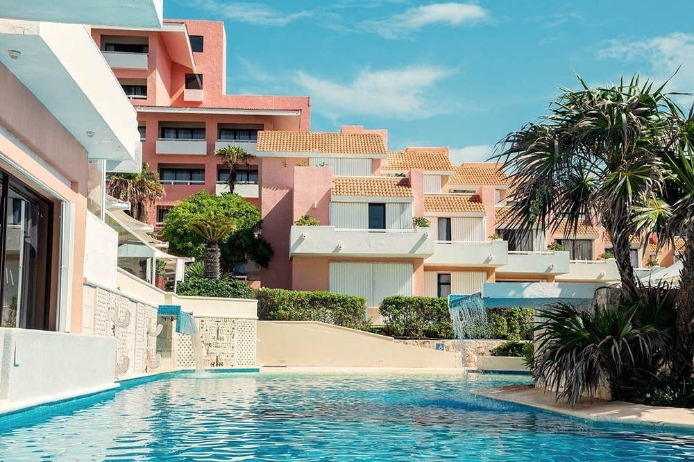 una piscina rodeada de palmeras frente a un edificio rosa