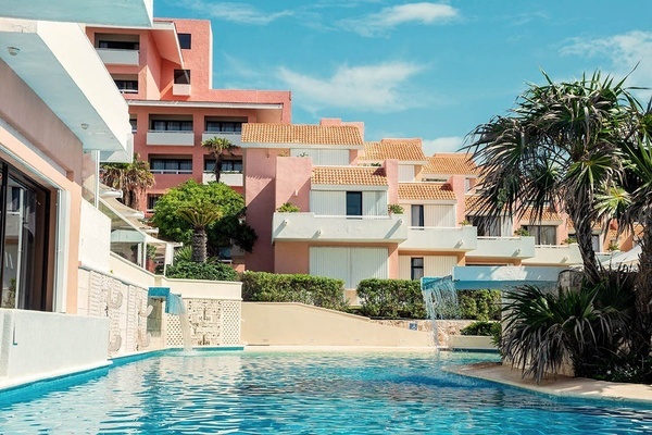 una piscina rodeada de palmeras frente a un edificio rosa
