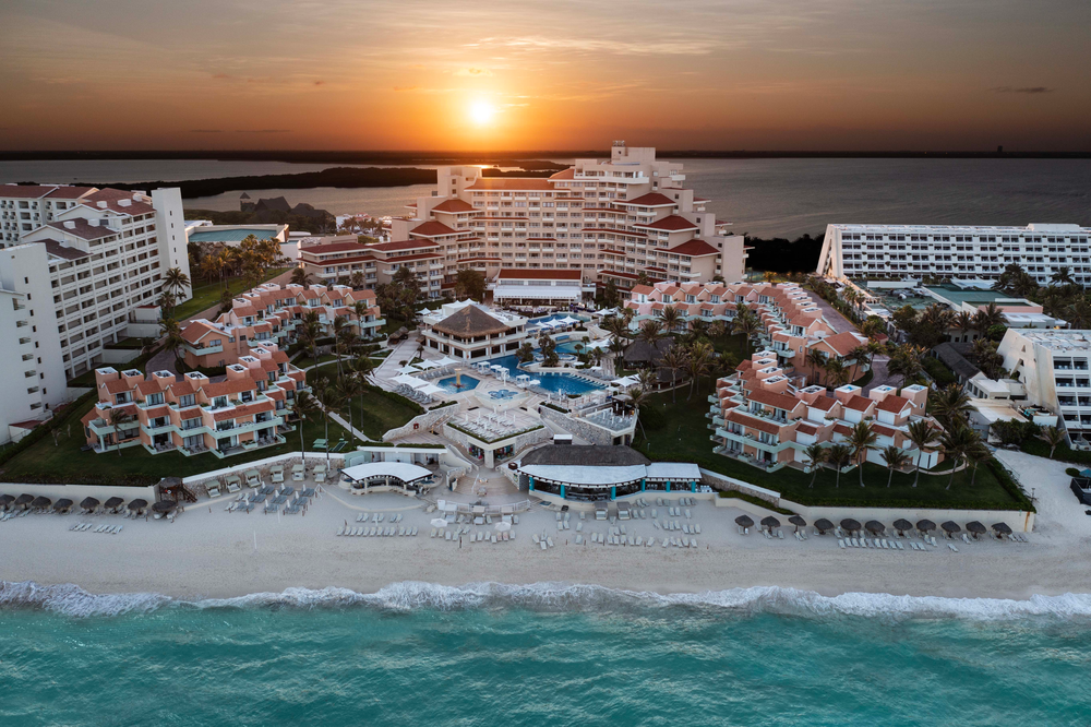 Resort de playa con arquitectura escalonada y piscinas, vistas al mar y al amanecer. Ideal para Wyndham Grand Cancún All Inclusive Resort & Villas.