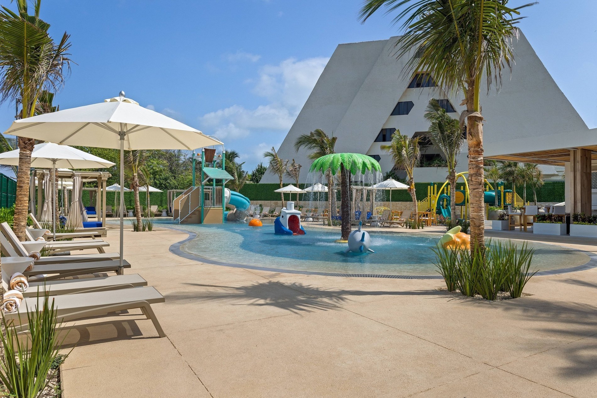 a swimming pool with palm trees and umbrellas in front of a building