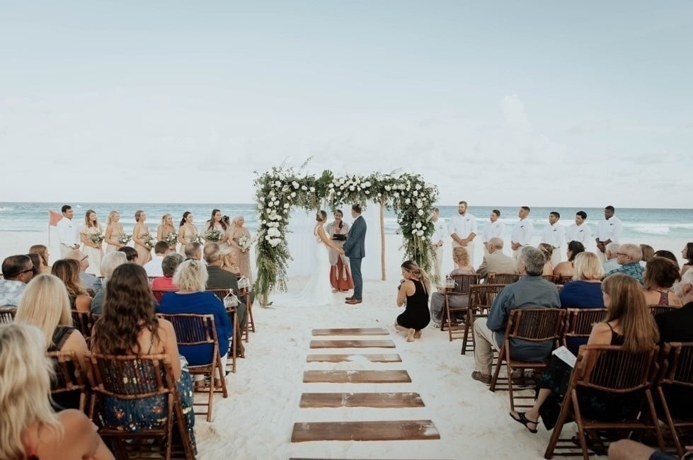 una novia y un novio se besan en la playa frente a un arco floral