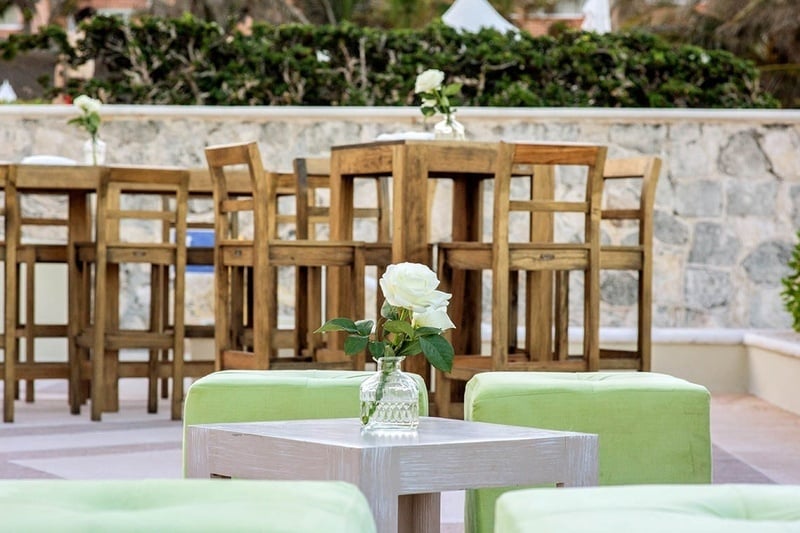 una mesa con un jarrón de rosas y taburetes verdes