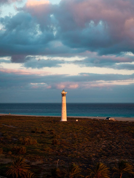 Une plage de sable clair avec une mer turquoise et des vagues écumantes sous un ciel bleu parsemé de nuages.