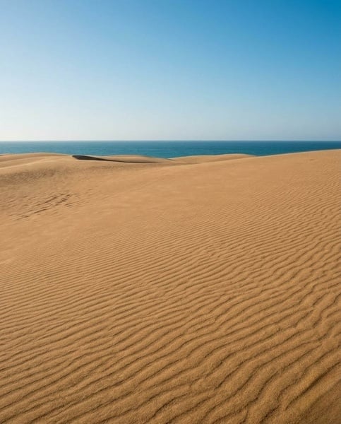 Une plage de sable clair avec une mer turquoise et des vagues écumantes sous un ciel bleu parsemé de nuages.