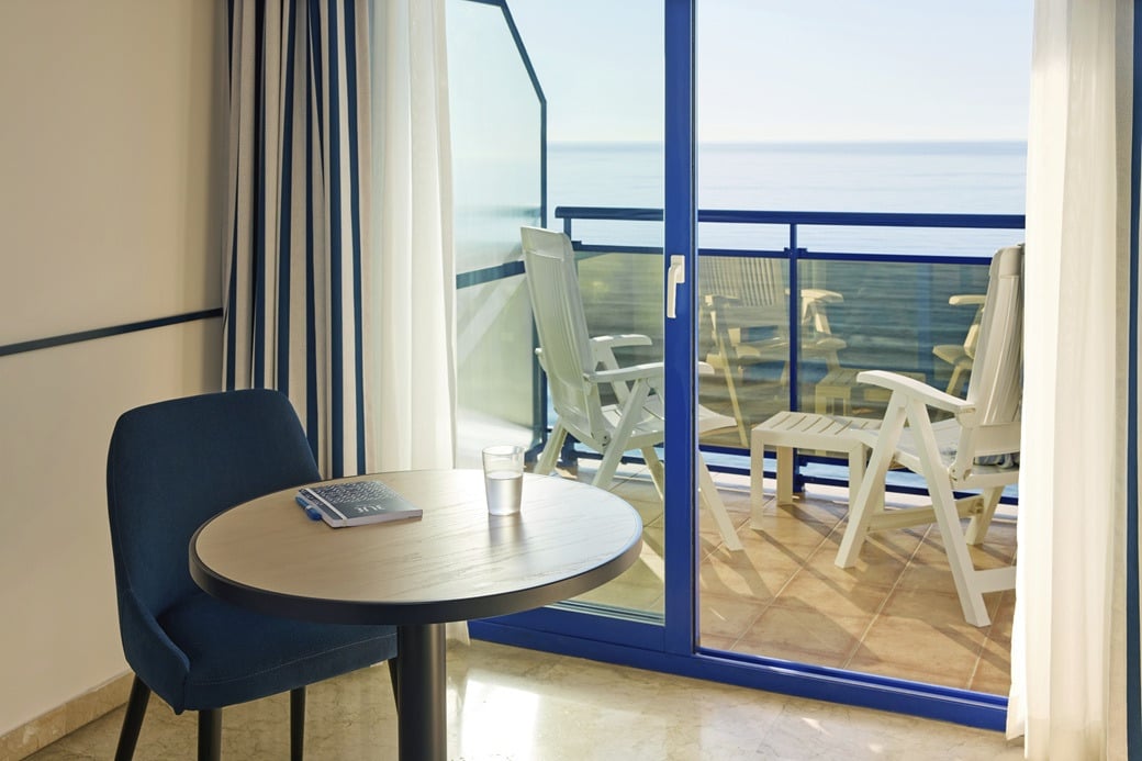 Balcony with ocean view, chairs, table, and glass of water. Hotel roomYaramar.