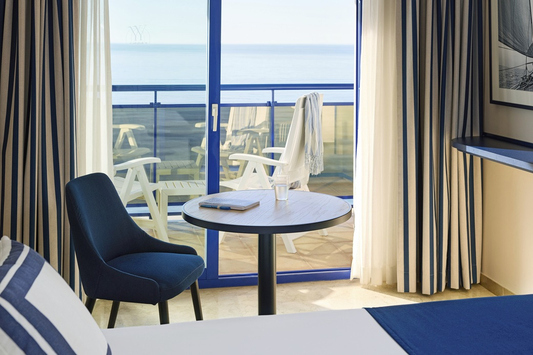 Balcony Yaramar with ocean view, navy chair, and striped curtains.