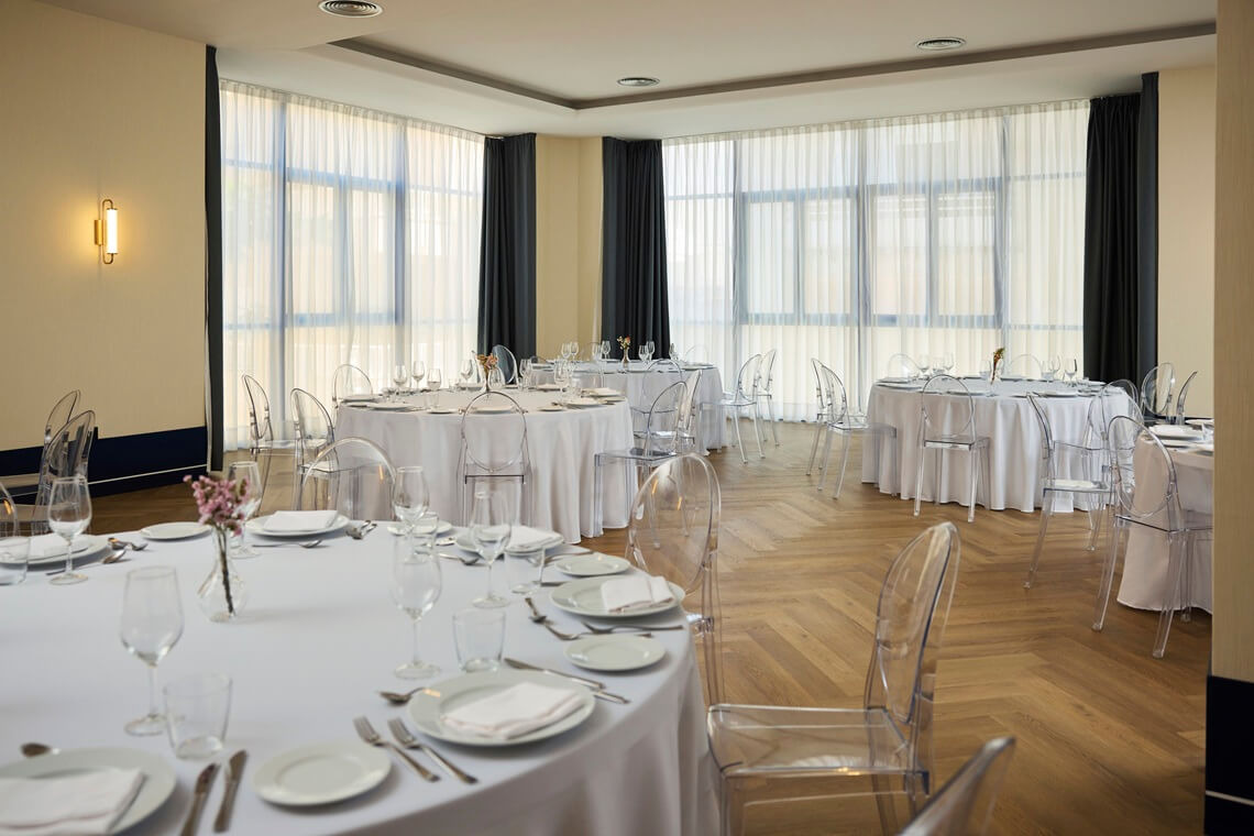 Elegant event space with round tables, clear chairs, and large windows, perfect for Yaramar.