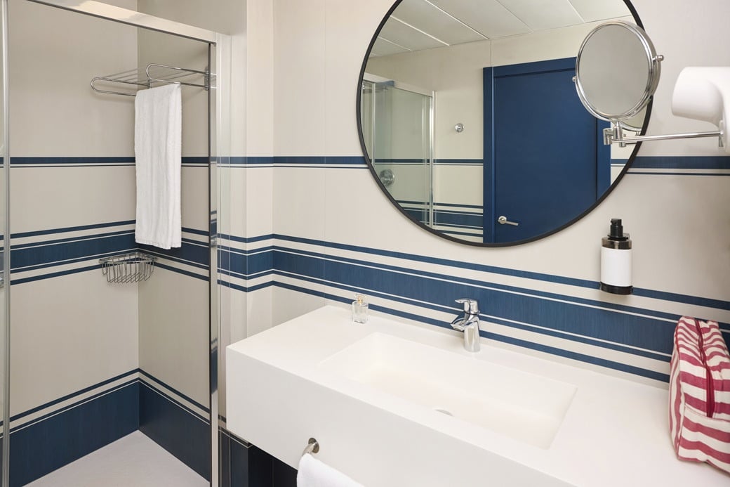 Modern hotel bathroom with white sink, blue striped walls, and shower. Yaramar