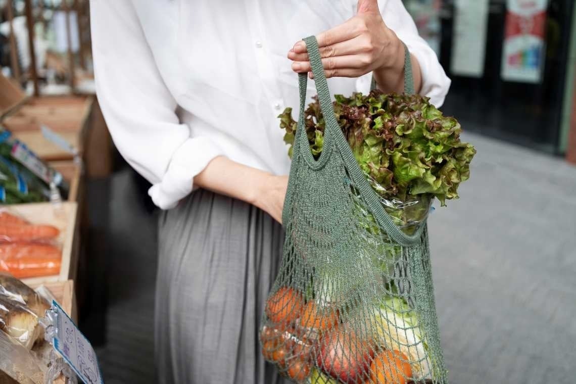 una mujer sostiene una bolsa de malla llena de frutas y verduras .