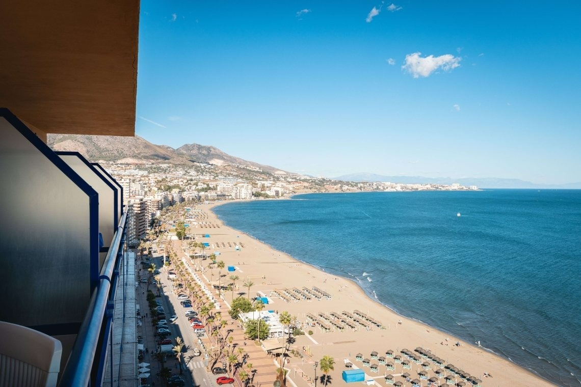 a view of a beach from a balcony with mountains in the background