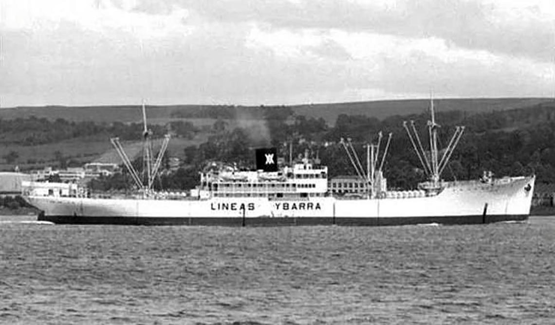 Fotografía en blanco y negro de un barco de carga, el 'LINEAS YBARRA', navegando en el agua con un paisaje boscoso de fondo.