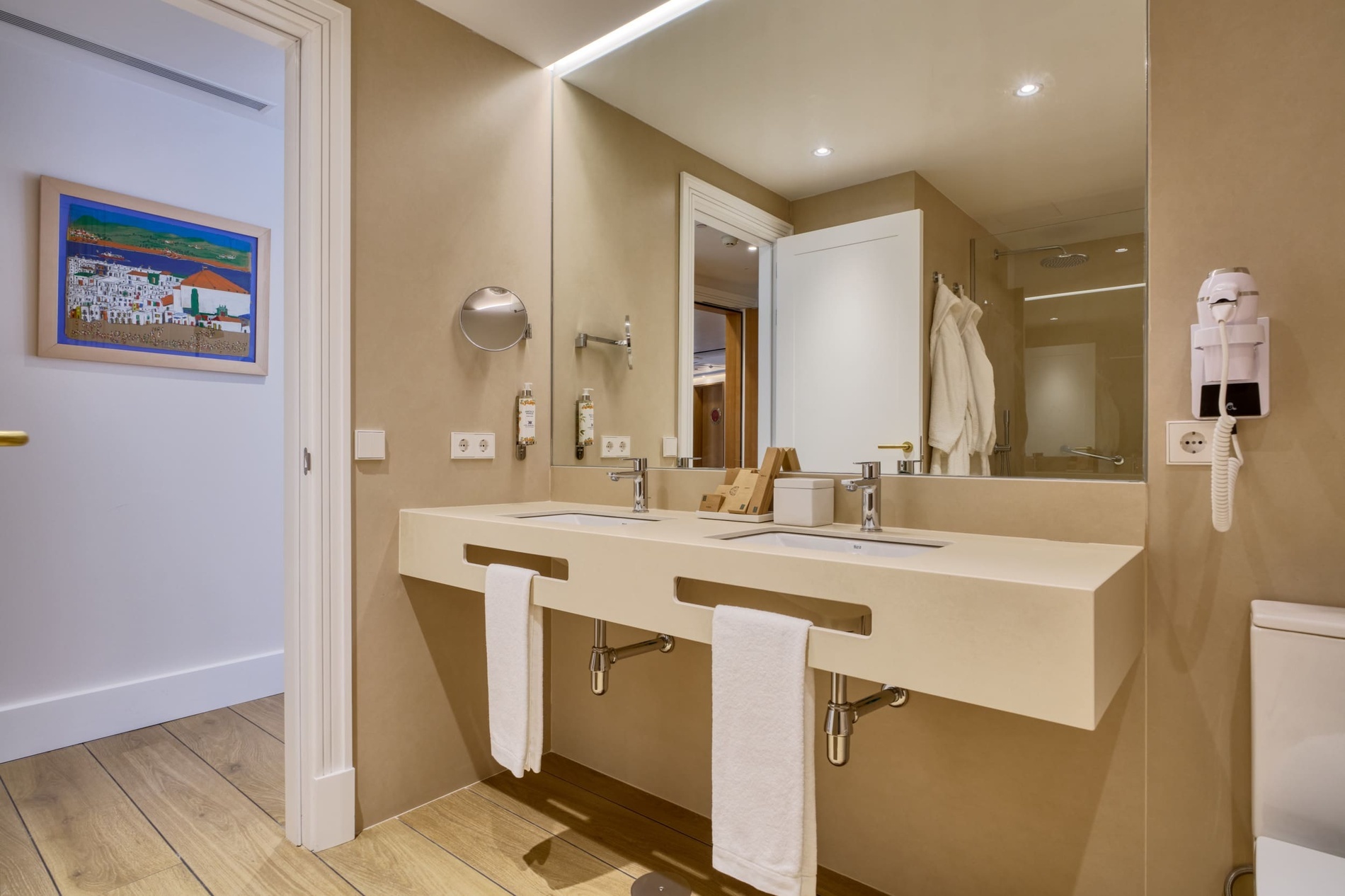 Modern double vanity bathroom with artwork, robes, and hairdryer at Ybarra Sevilla.