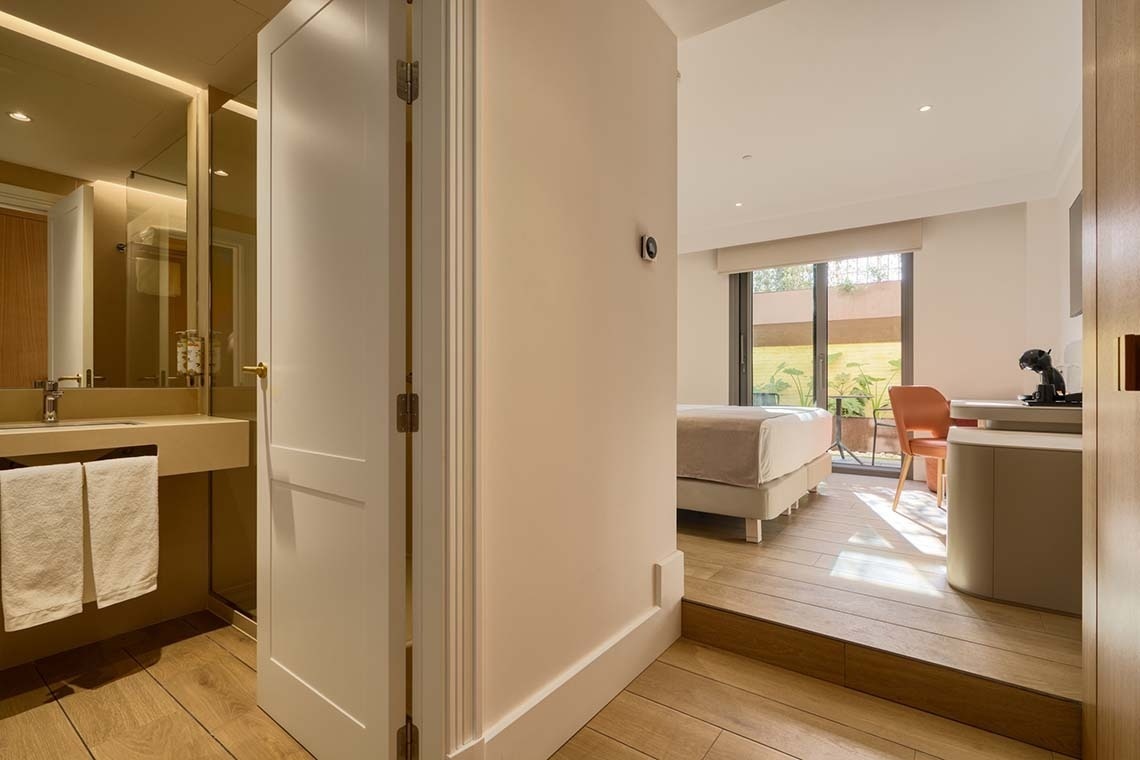 Se muestra un interior moderno con un baño visible a través de una puerta abierta y un dormitorio luminoso con acceso a un patio exterior.