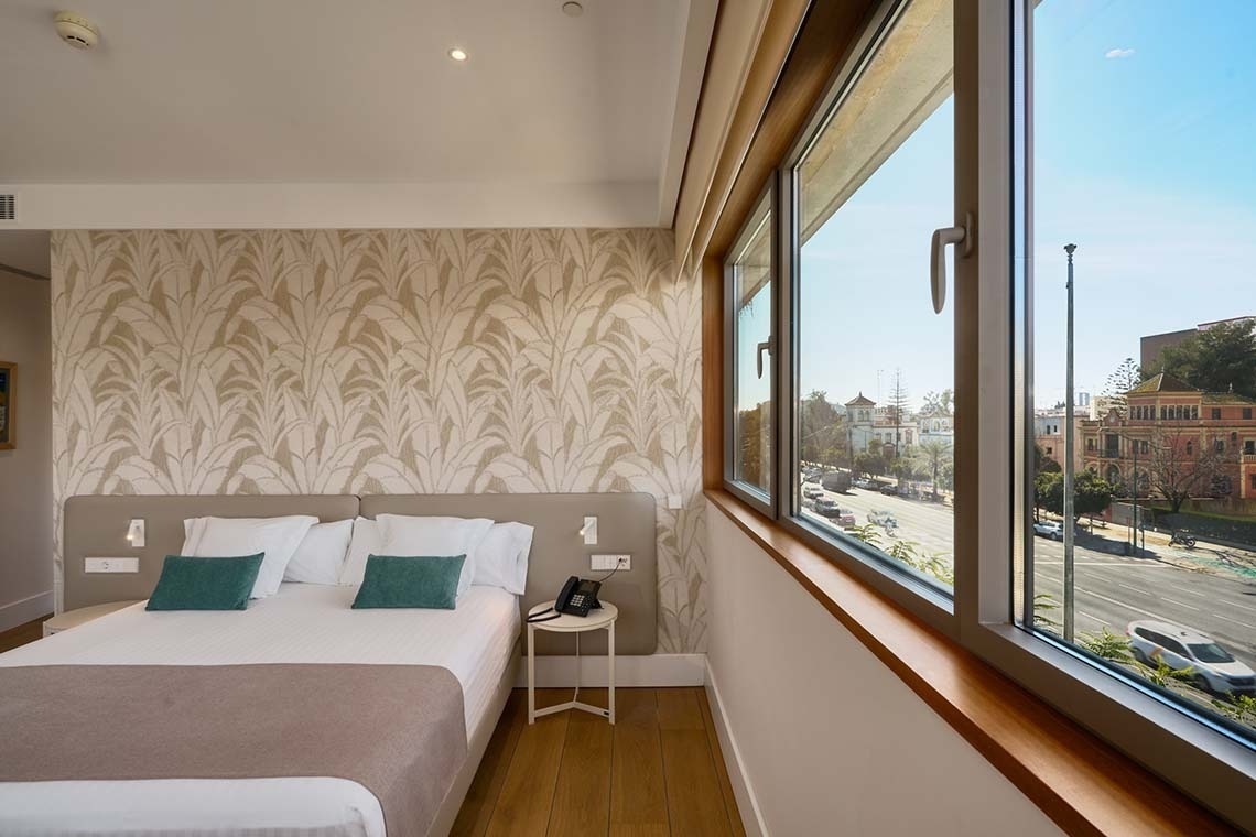 Una habitación de hotel moderna con una cama doble, papel tapiz estampado y una gran ventana con vistas a una concurrida calle de la ciudad.