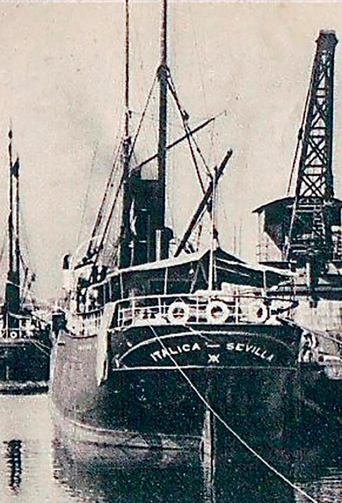 La imagen muestra la popa del buque 'Itálica' con su puerto de origen 'Sevilla' visible, atracado en un puerto junto a otro barco y una grúa.