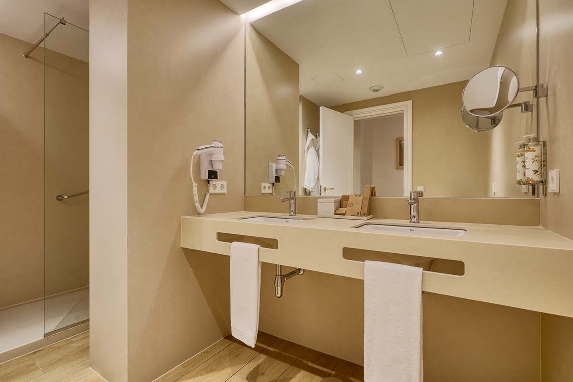 Un moderno y luminoso baño con un tocador doble, un gran espejo y una ducha acristalada.