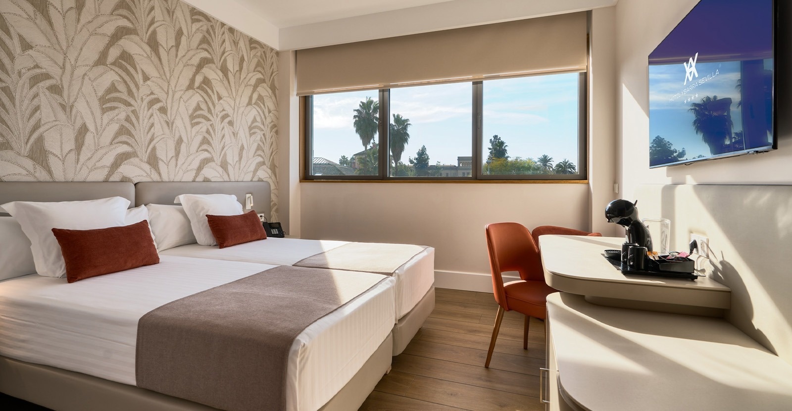 Una moderna habitación de hotel con una cama doble, un gran ventanal que da al exterior y una pared decorada con papel tapiz de hojas.