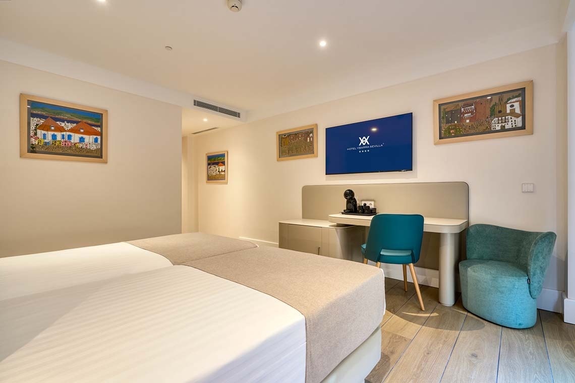 Una luminosa y moderna habitación de hotel equipada con dos camas, un escritorio, un televisor y coloridas obras de arte.