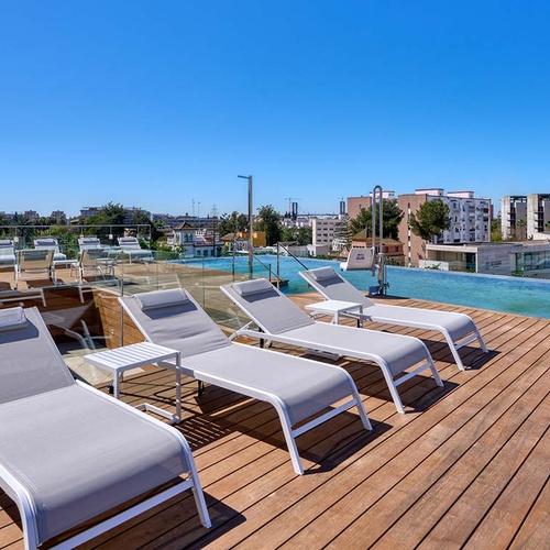 Relax on Ybarra Sevilla hotel's rooftop deck with infinity pool and lounge chairs.
