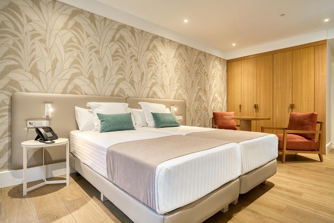 Se muestra una moderna y luminosa habitación de hotel con dos camas, un televisor, un escritorio y acceso a un balcón.