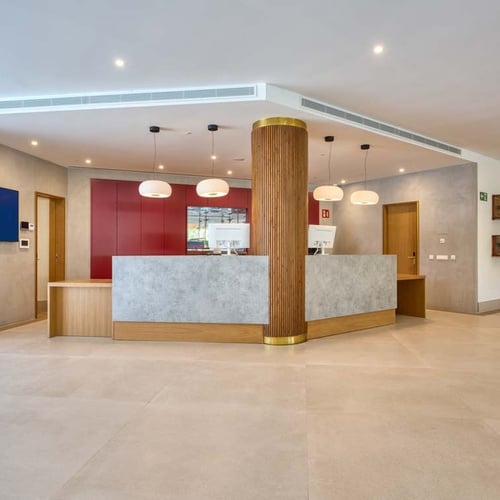 Modern reception desk at Hotel Ybarra Sevilla with concrete counter and pendant lights.