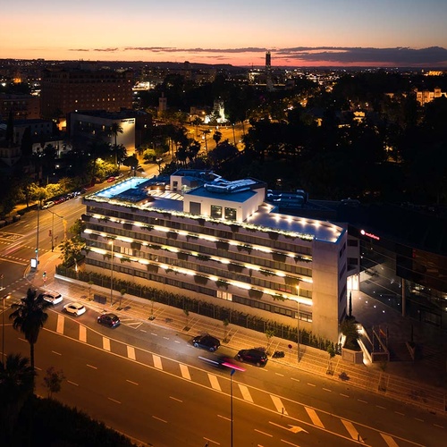 Modern hotel exterior at dusk, Ybarra Sevilla, with city lights and cars.